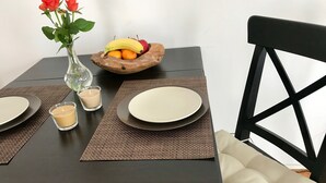 Una mesa de comedor con un jarrón de rosas rojas, un frutero y dos velas.