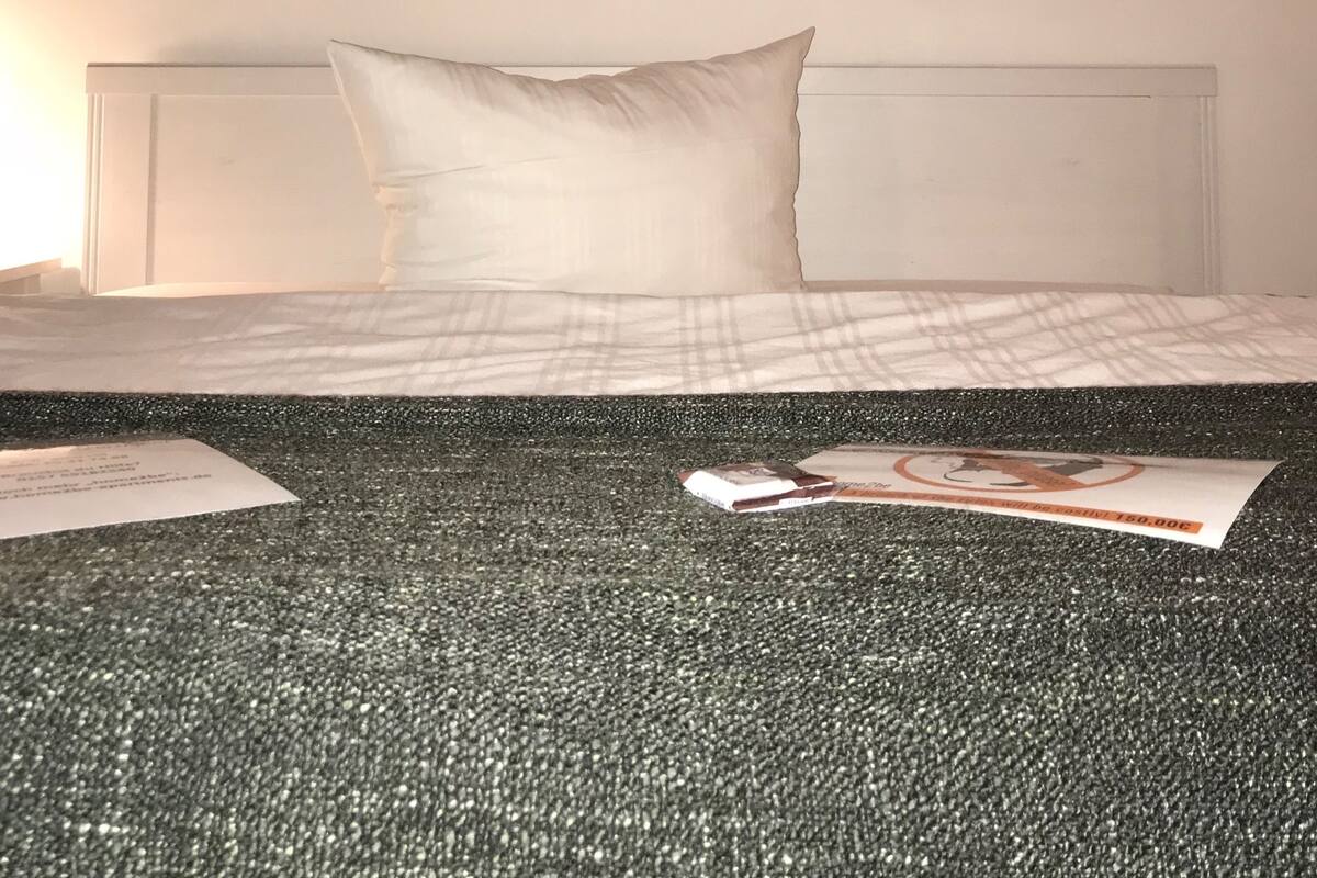Ett hotellrum med en säng, en kudde, en affisch på väggen och en tidning på golvet.