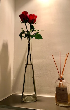 Un vaso di vetro trasparente con una singola rosa rossa e una bottiglia di colonia FIAMARE su uno scaffale.
