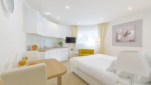 A hotel room with a bed, a desk with a chair, a small table with two glasses of orange juice, a TV, and a painting on the wall. - Best Location Apartments (Split)