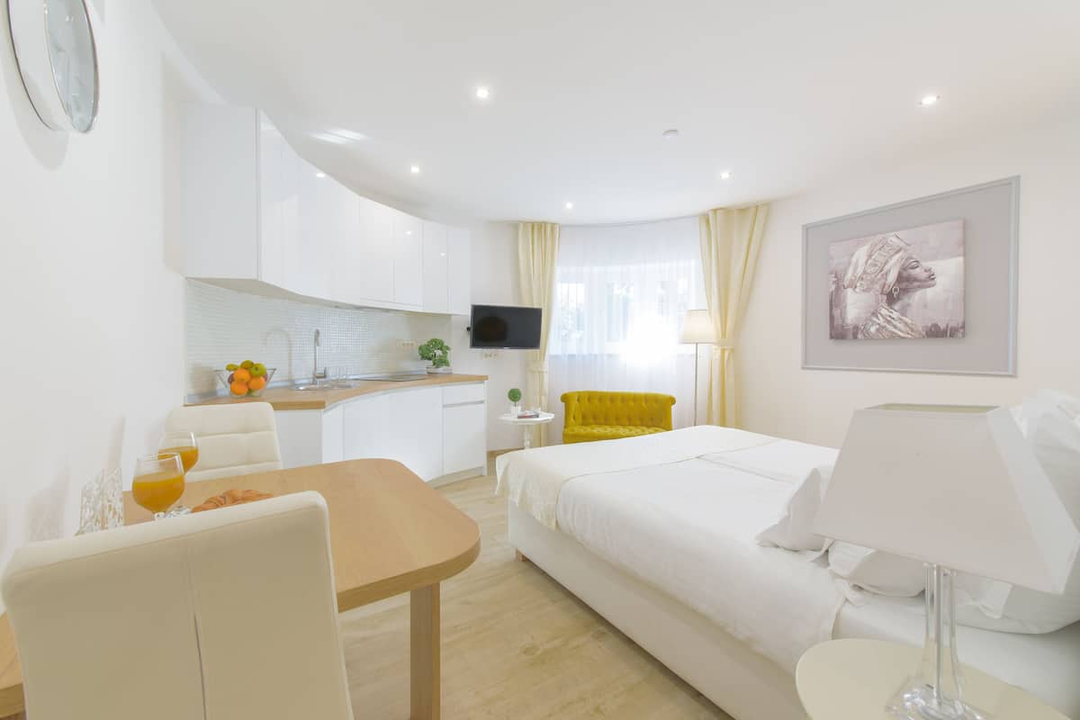 Quarto de hotel com uma cama, uma escrivaninha com cadeira, uma mesinha com dois copos de sumo de laranja, uma televisão e um quadro na parede.