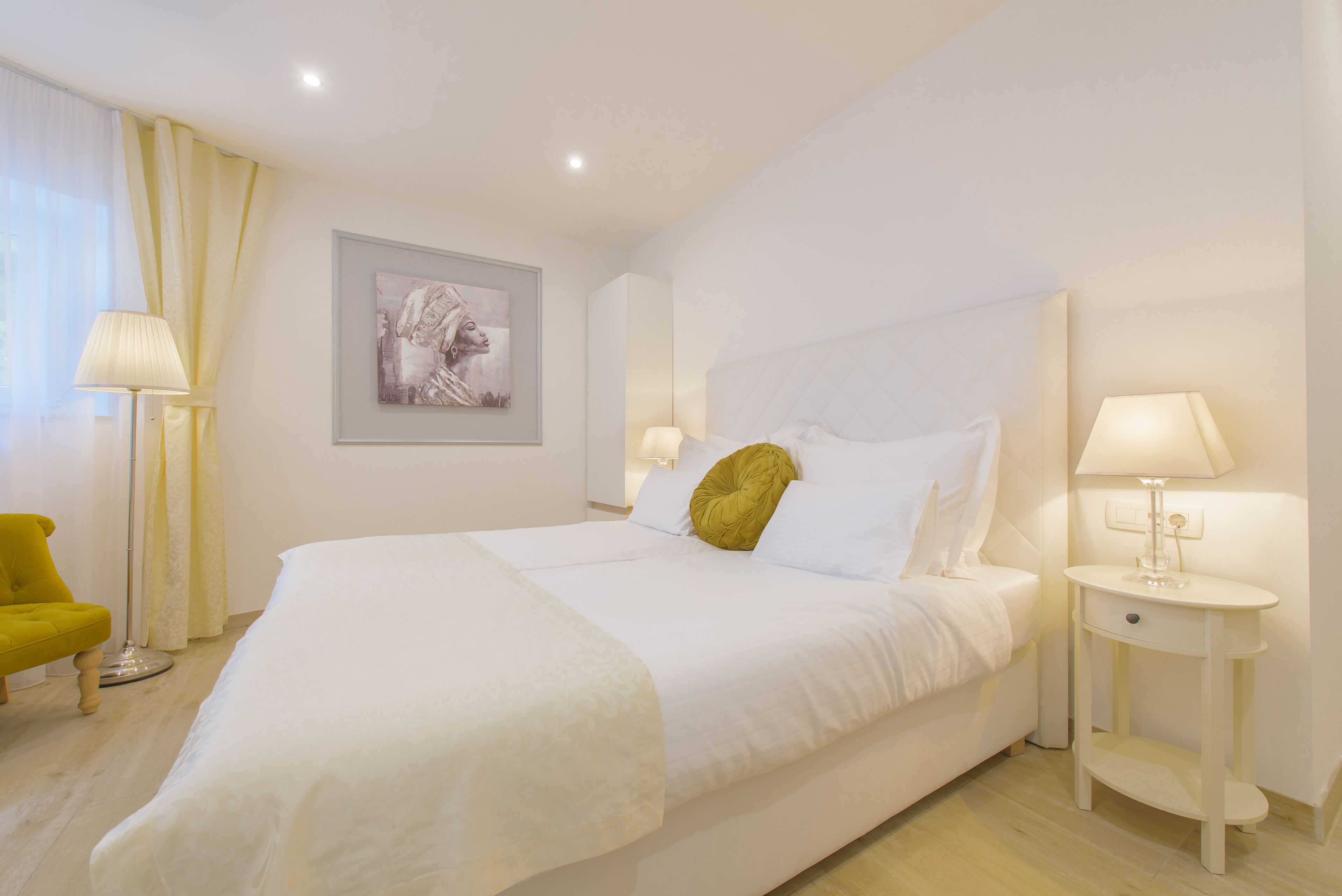 A neatly arranged hotel room with a large bed, bedside lamps, a small table, and a chair.