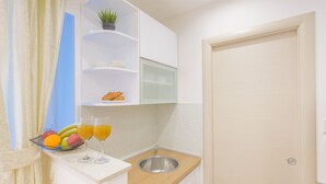 A compact kitchenette with a fruit bowl, two glasses of orange juice, a sink, and a small shelf with a plant and a cup. - Best Location Apartments (Split)