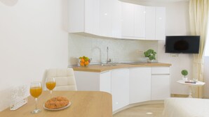 A modern kitchen with white cabinets, a wooden countertop, and a dining area with a table set for two. - Best Location Apartments (Split)