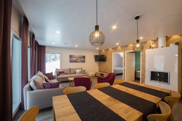 A modern living room with a sofa, red chairs, a dining table, and a TV mounted on the wall.