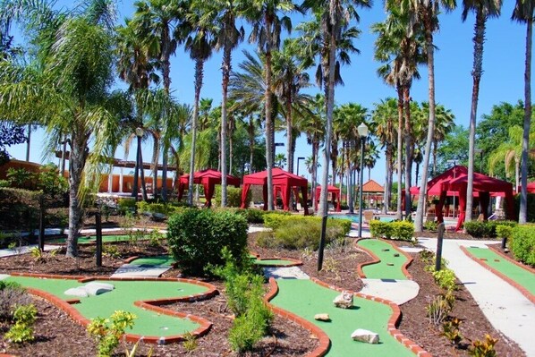 A miniature golf course with red tents and palm trees.