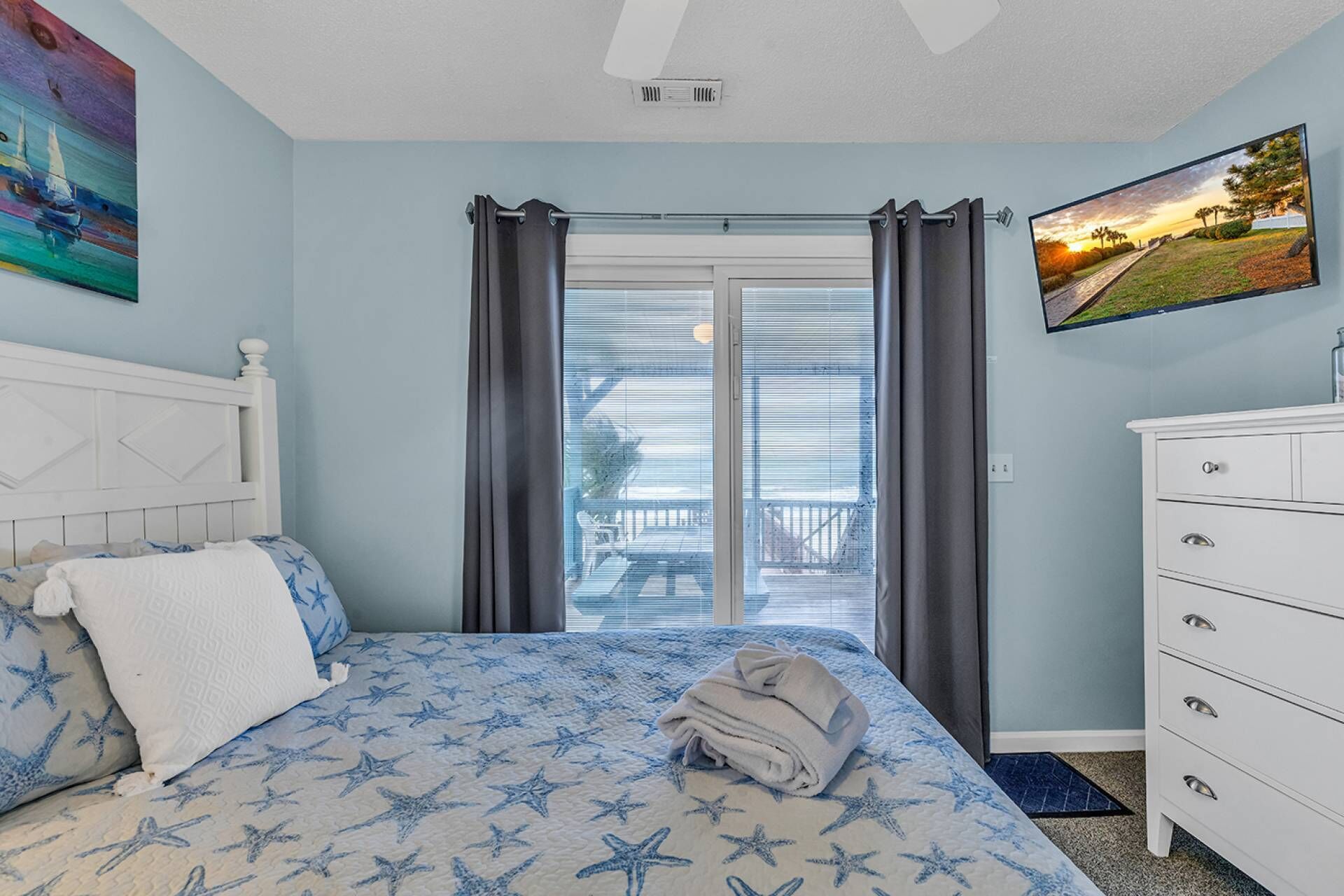 A bedroom with a bed, a dresser, a painting, and a view through the window.