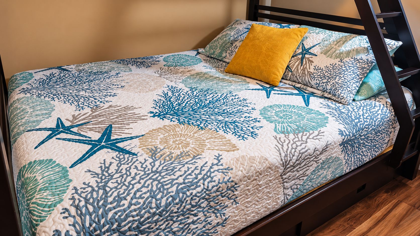 A bed with a patterned bedspread featuring coral and starfish designs, a yellow pillow, and a black metal frame.