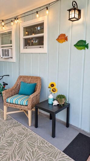 A wicker chair with a striped cushion, a small table with a vase of sunflowers, and decorative fish on a wall. - 5 O'Clock Somewhere getaway-Walk/Bike to Beach,Shops ,Fenced private doggie area (Naples)