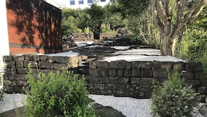 Um jardim com muro de pedra, caminho de cascalho e diversas plantas.