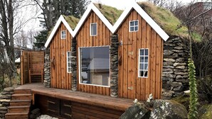 Uma cabana de madeira com parede de pedra, uma janela grande e um deck de madeira.