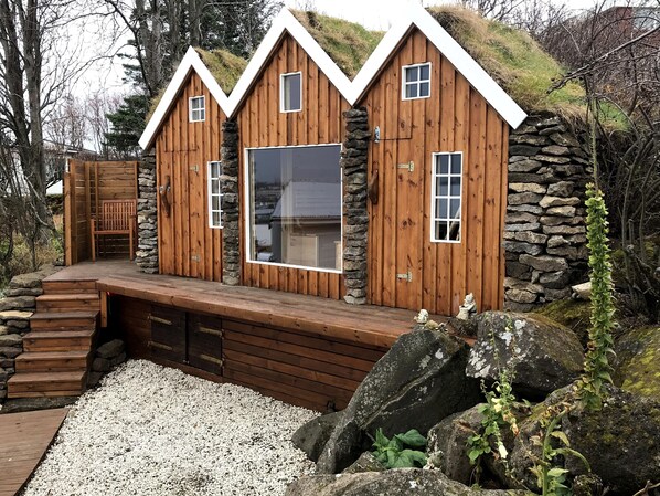 Eine Holzhütte mit Steinwand, großem Fenster und einer Holzterrasse.