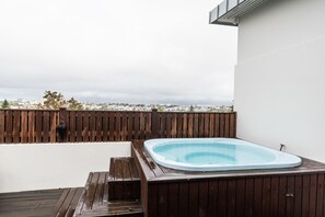 Ein Whirlpool auf einer Holzterrasse mit Blick auf die Stadt im Hintergrund.