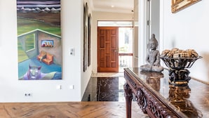 Um corredor com piso de madeira, piso de mármore, porta de madeira e uma estátua sobre uma mesa.