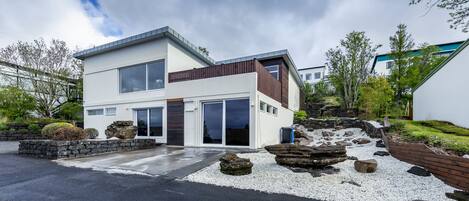 Ein modernes, zweistöckiges Haus mit Flachdach, großen Fenstern und einem Steinweg zum Eingang.