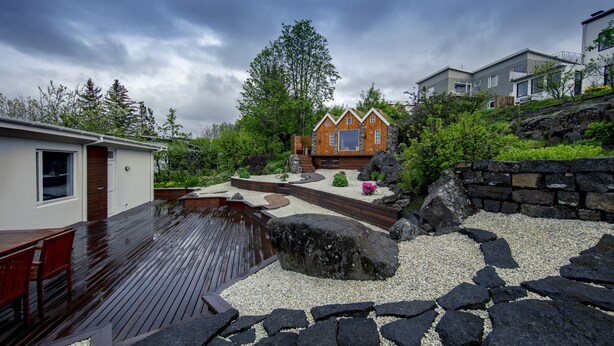 Uma casa moderna com um deck de madeira, um caminho de pedra e um pequeno lago.