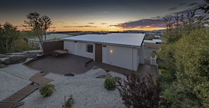 Ein modernes Haus mit einer Terrasse, einem kleinen Garten und Blick auf den Sonnenuntergang über dem Wasser.