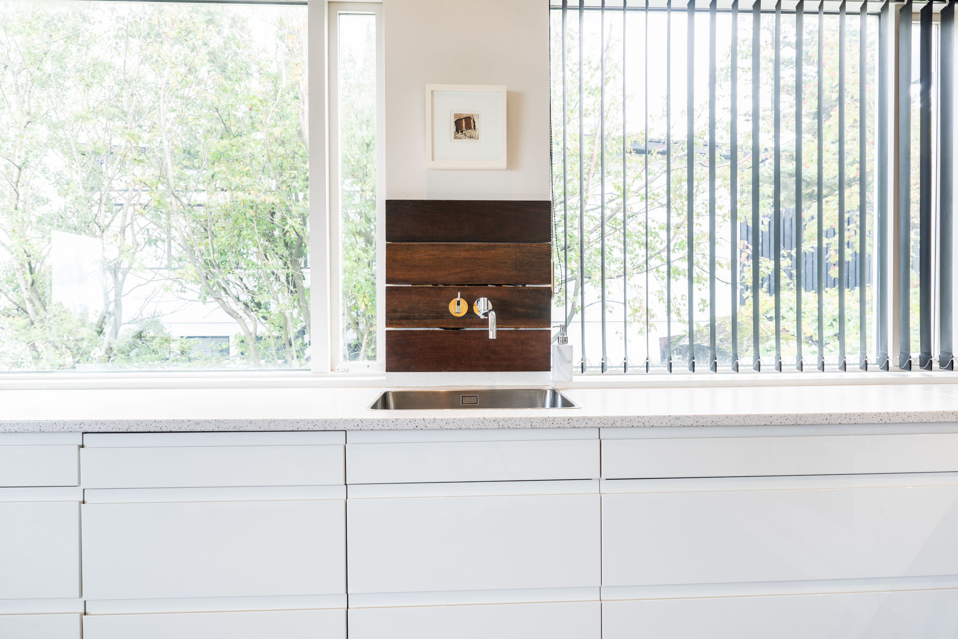 Una cocina con gabinetes blancos, un lavamanos de acero inoxidable y una ventana con vista a árboles.