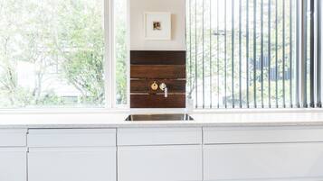 Una cocina con gabinetes blancos, un lavamanos de acero inoxidable y una ventana con vista a árboles.