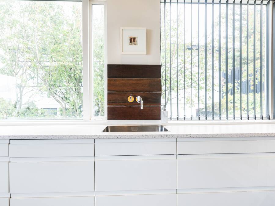 Una cocina con gabinetes blancos, un lavamanos de acero inoxidable y una ventana con vista a árboles.