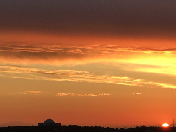 Un atardecer con la silueta de un edificio y una estructura en forma de cúpula contra un cielo de tonos naranja y amarillos.