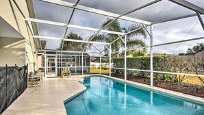 A covered swimming pool with a clear view of the surrounding landscape, including palm trees and a hedge. - Clermont Home w/ Pool & Game Room: 10 Mi to Parks! (Clermont)