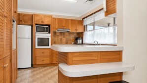 A kitchen with wooden cabinets, a microwave, a refrigerator, and a window with a curtain. - Hunter Valley Pool & Views, Sleeps 8 (Cessnock)