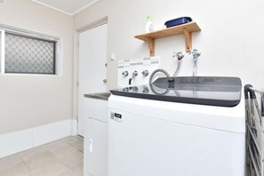 A laundry room with a washing machine, a dryer, and a shelf with bottles. - Book Direct for Accom with Pool in Hunter Valley (Cessnock)