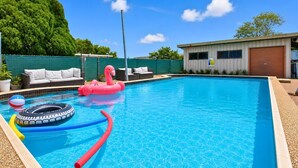 Una piscina con juguetes inflables, un área de descanso con mobiliario exterior y un edificio al fondo.