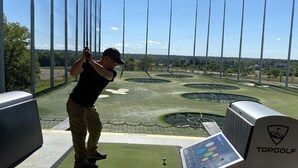 Un campo de prácticas de golf con área delimitada por redes, zona de salida y marcador electrónico.