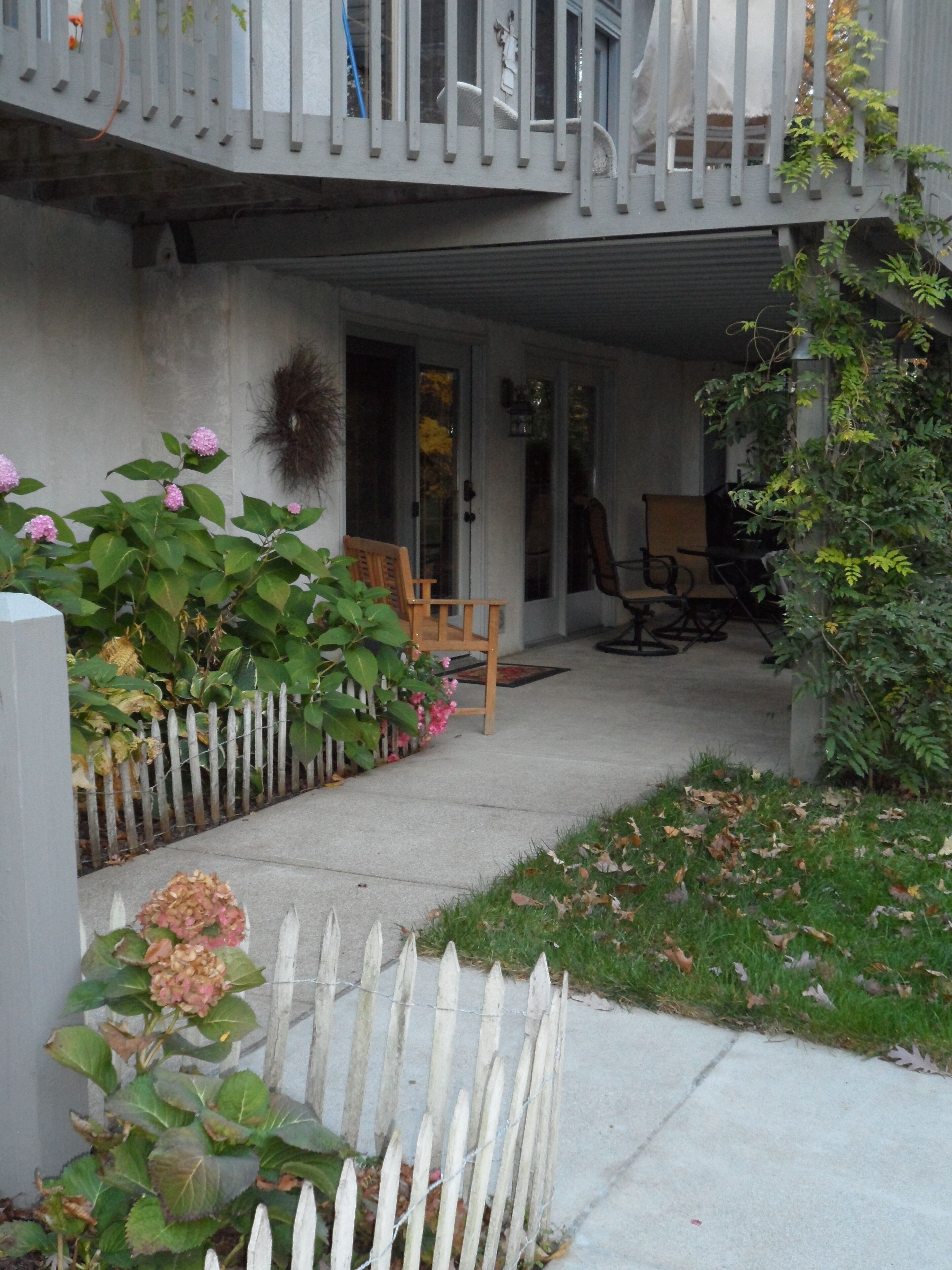 A residential building with a covered porch, a white picket fence, and a garden with pink flowers.