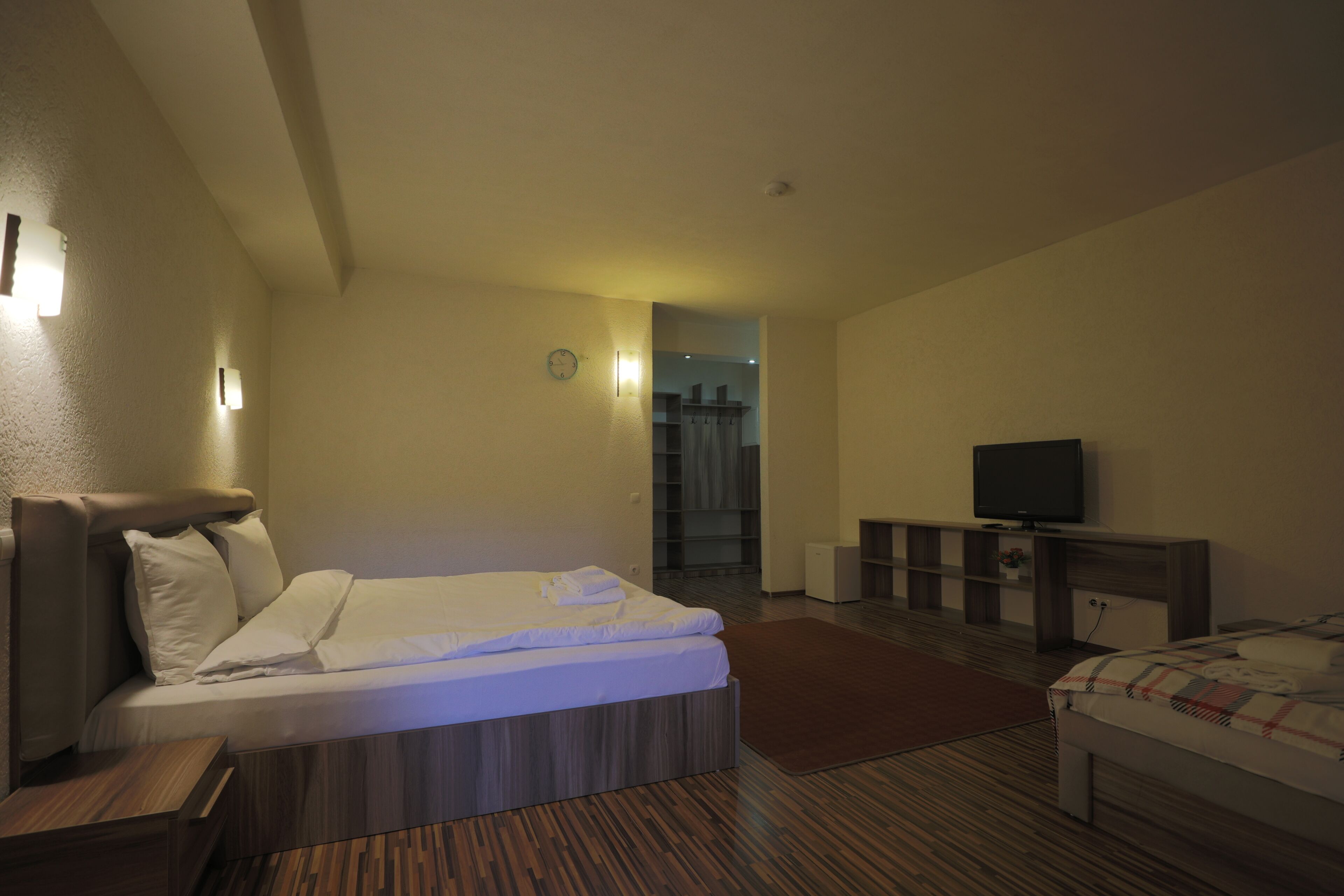 A hotel room with a bed, bedside table, TV, and a small seating area.