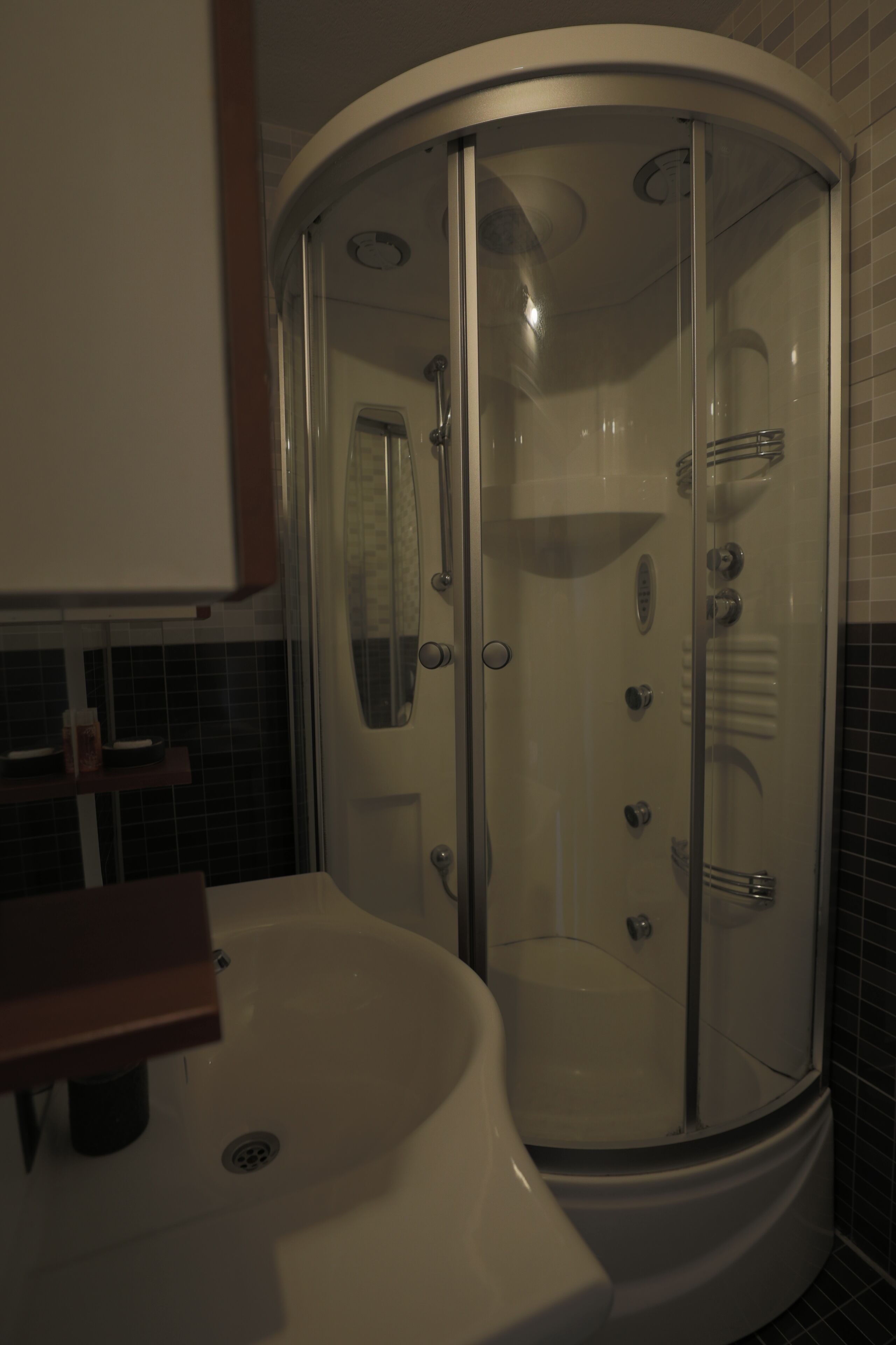 Un baño con ducha de mampara de vidrio, un lavabo blanco y pared de azulejos.