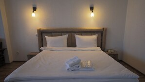 A neatly made bed with white linens, two bedside tables with lamps, and a wooden headboard. - Hotel Denis & Spa (Pristina)