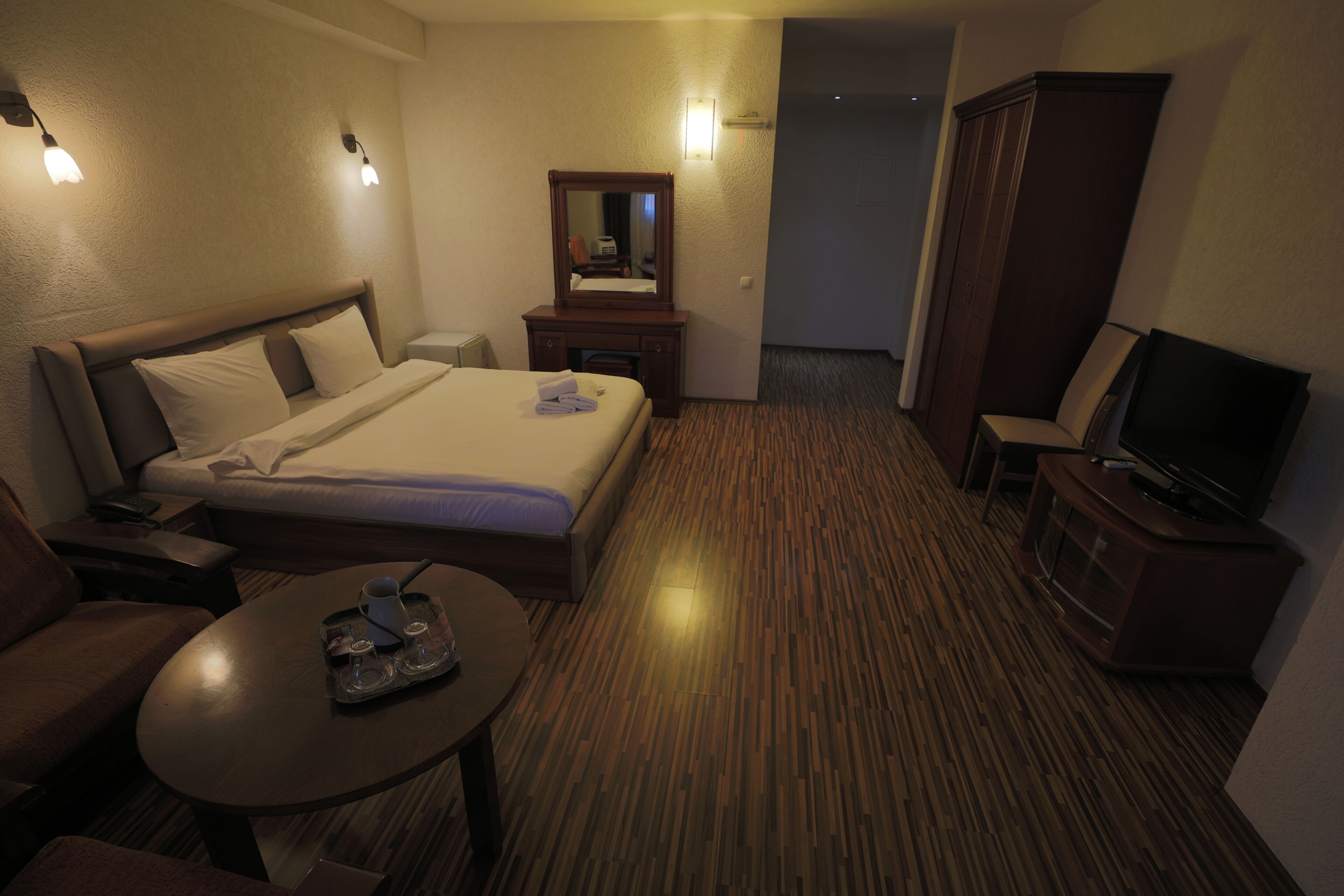 A hotel room with a bed, bedside table, TV, and a mirror.