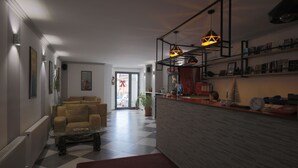 A modern living room with a checkered floor, a glass coffee table, and a red rug. There are two pendant lights above a wooden reception desk. - Hotel Denis & Spa (Pristina)