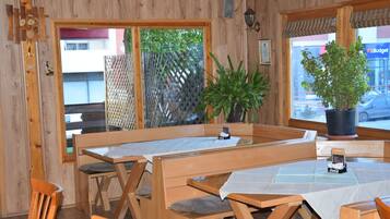 Un intérieur en bois avec des tables et des bancs, des plantes en pot et une vue sur l’extérieur.