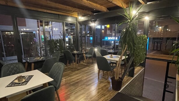 An indoor dining area with wooden flooring, tables, chairs, and potted plants. - Hotel Denis & Spa (Pristina)