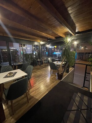 Un comedor interior con suelo de madera, mesas, sillas y plantas en macetas.