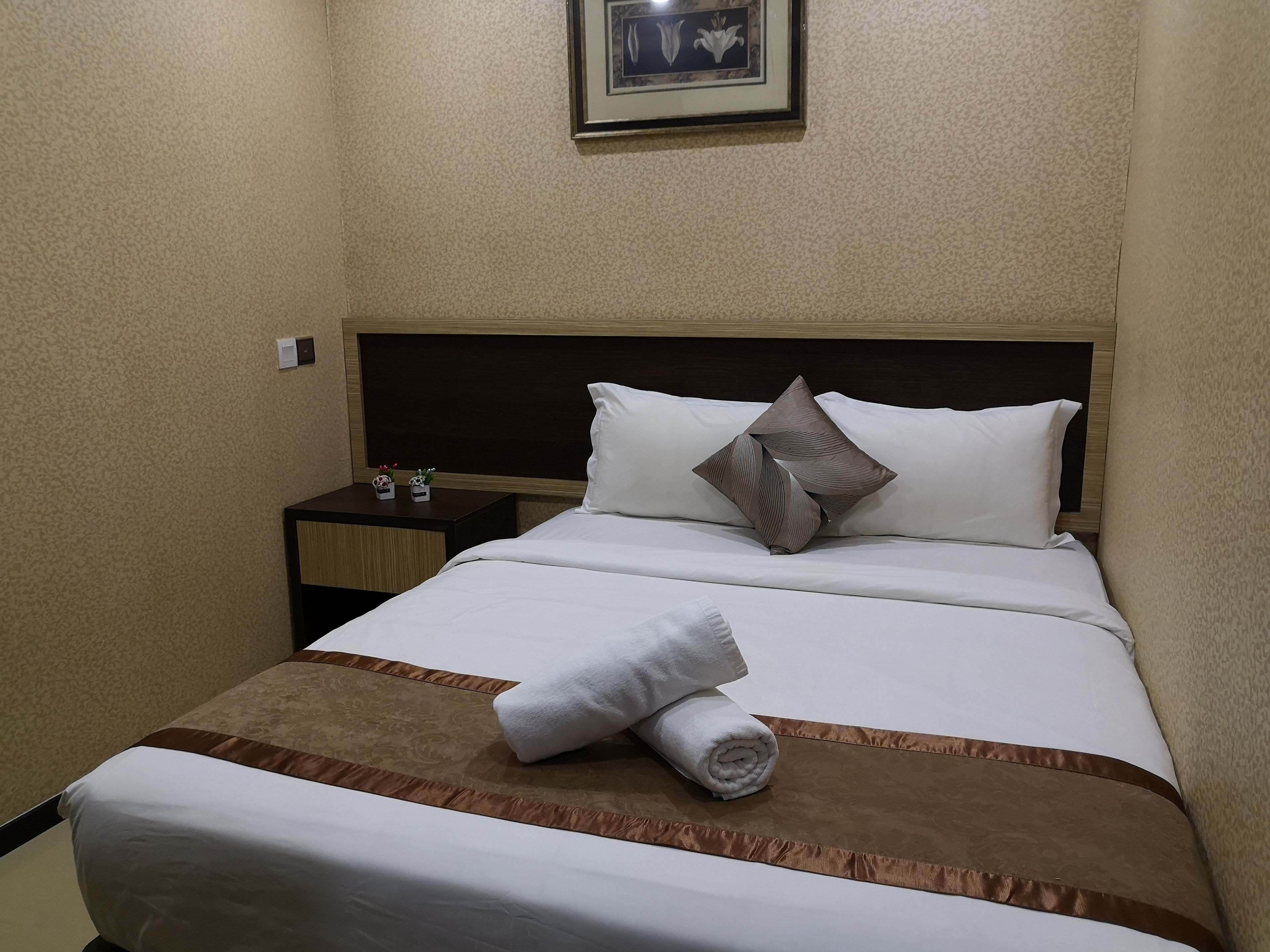 A neatly made bed with a brown accent, a white pillow, and a rolled towel on the footboard.