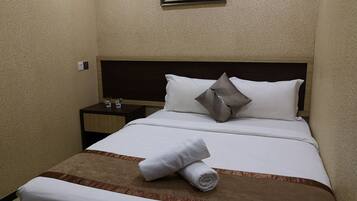 A neatly made bed with a brown accent, a white pillow, and a rolled towel on the footboard.