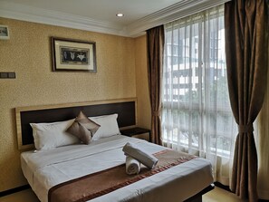 Ein Hotelzimmer mit einem ordentlich bezogenen Bett, einem gerahmten Bild an der Wand und einem Fenster mit Vorhängen.