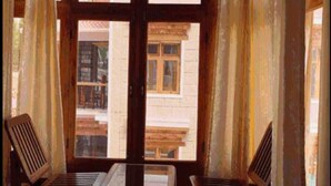 A room with two wooden chairs and a table, large windows with curtains, and a view of buildings outside. - Hotel Om Ladakh (Leh)