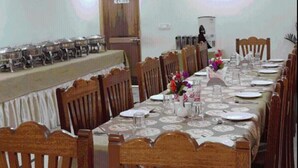 A long dining table with chairs, a buffet setup on the left, and a wooden cabinet in the background. - Hotel Om Ladakh (Leh)