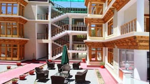 A multi-story building with a central courtyard featuring outdoor seating and potted plants. - Hotel Om Ladakh (Leh)