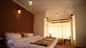 A bedroom with a large bed, a wooden headboard, and a window with curtains. - Hotel Om Ladakh (Leh)