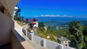 A hotel with a mountain view, a red-roofed building, and a road with vehicles. - Uttarakhand Resort (Somashwar)