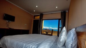 A hotel room with a large bed, a television mounted on the wall, and a window offering a view of the sky and clouds. - Uttarakhand Resort (Somashwar)