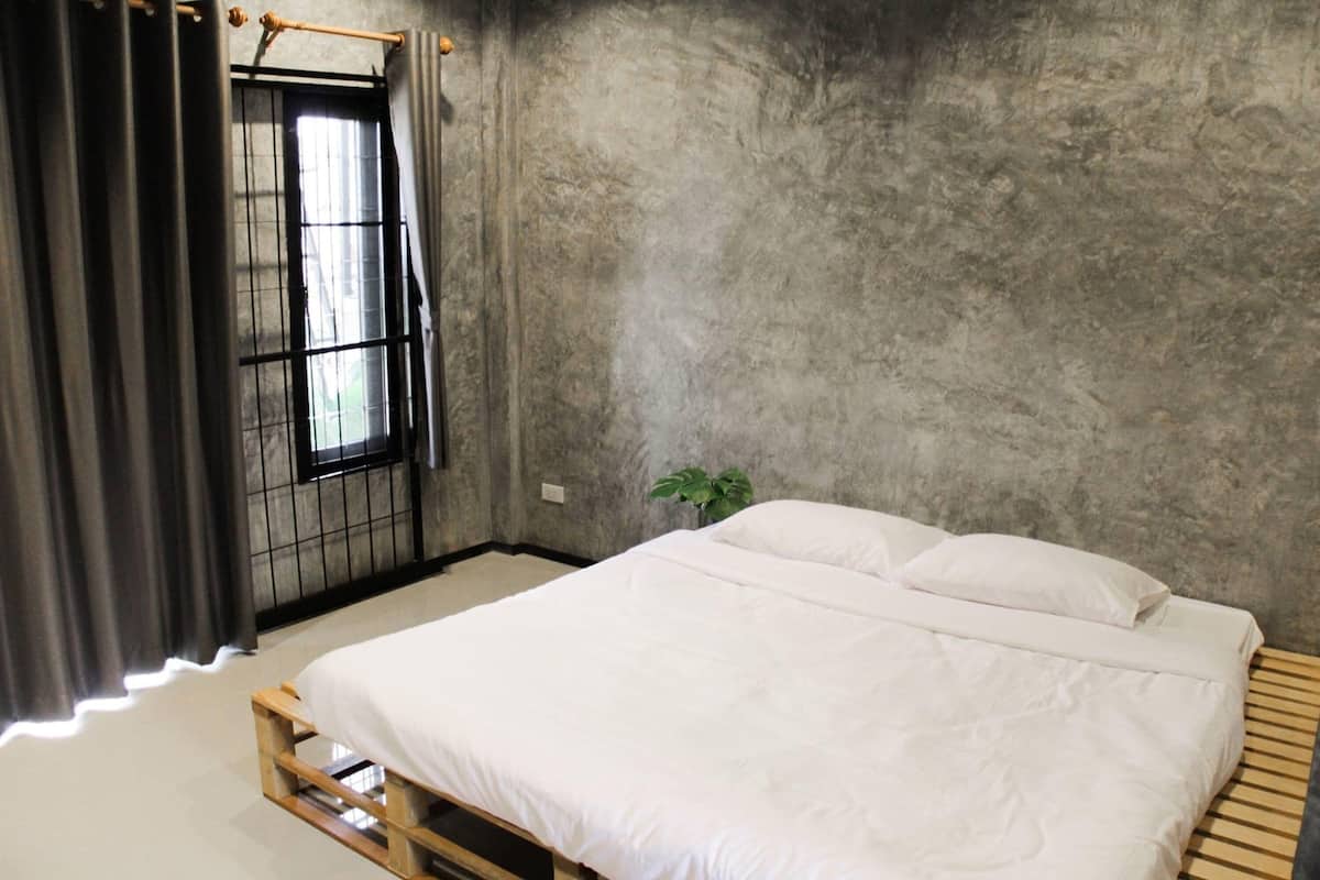A bedroom with a bed, a window with a metal grid, and a plant.