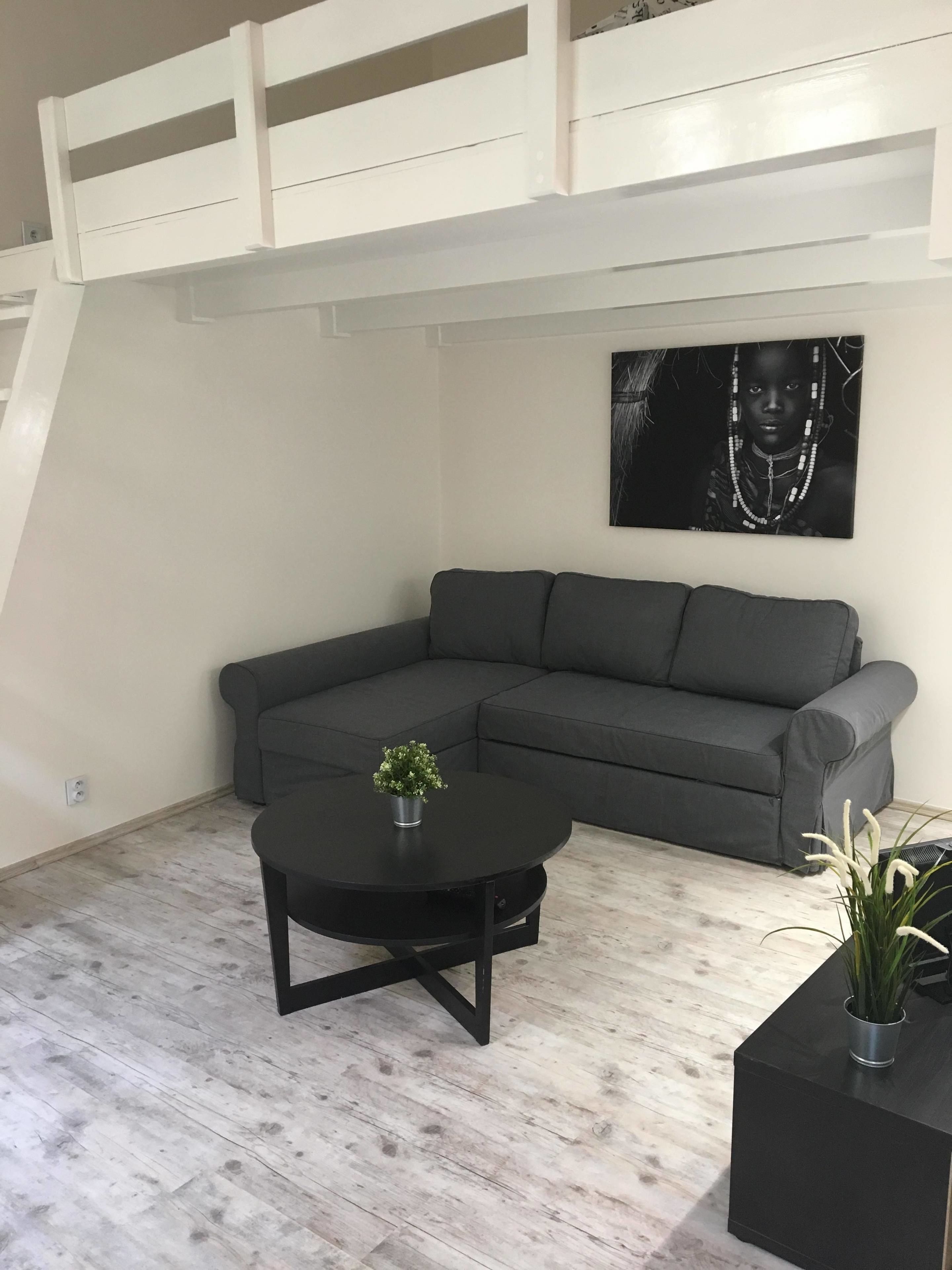 Un moderno loft con un divano angolare grigio, un tavolino nero e una piccola pianta in vaso.